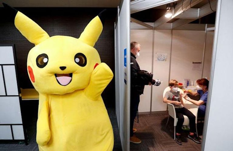 موظف طبي يرتدي زي سوبرمان ينظر إلى طفل يتلقى لقاح كورونا 