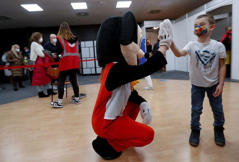 موظف طبي يرتدي زي سوبرمان ينظر إلى طفل يتلقى لقاح كورونا