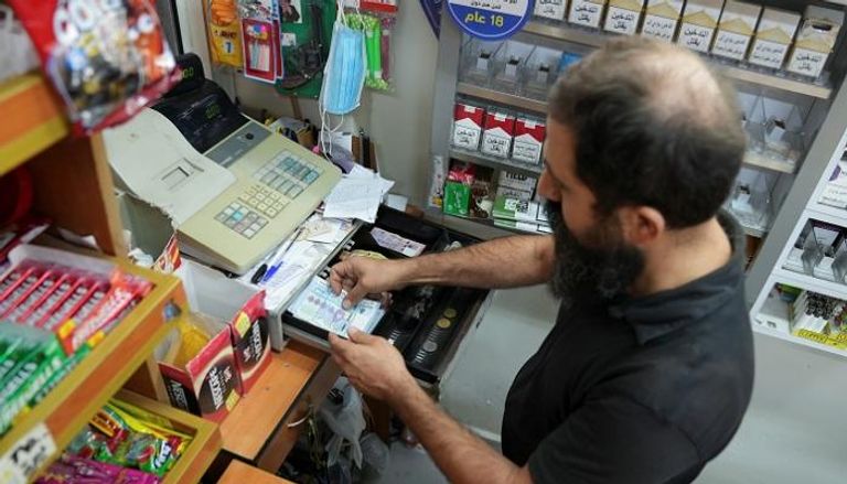 بائع يمسك بعملات ورقية من الليرة في متجر بالعاصمة بيروت