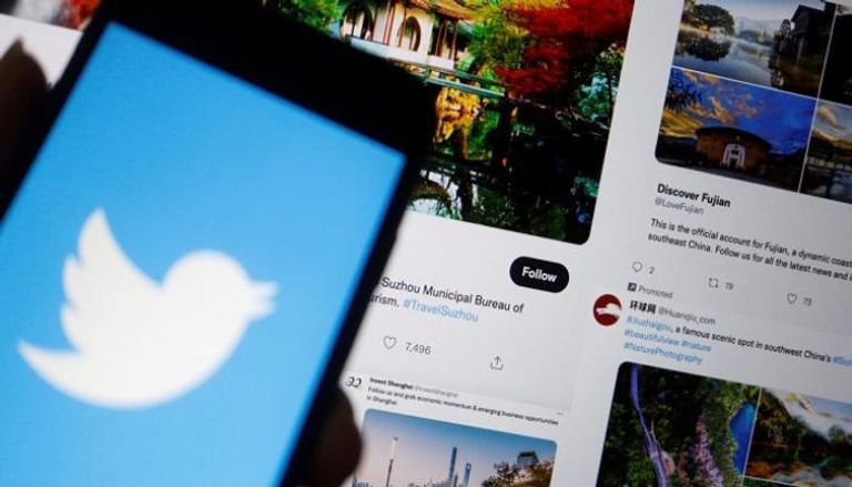 شعار تويتر على هاتف محمول بالقرب من شاشة كمبيوتر تُظهر بعض التغريدات - رويترز