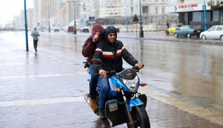 شابان يستقلان دراجة نارية بينما يحتميان من الأمطار في مصر- أرشيفية