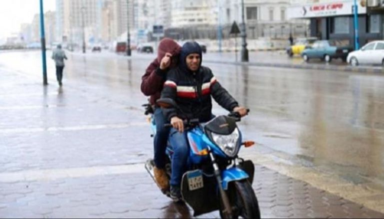 شابان يستقلان دراجة نارية بينما يحتميان من الأمطار في مصر- أرشيفية