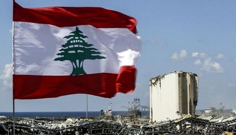 علم لبنان وفي الخلفية آثار سابقة لكارثة انفجار مرفأ بيروت