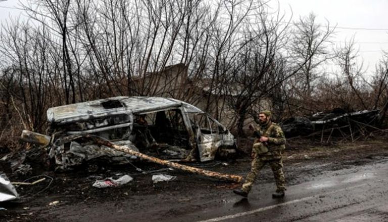 جندي أوكراني بجوار سيارة مدمرة