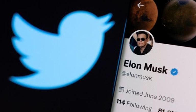 حساب Elon Musk على Twitter على هاتف ذكي أمام شعار تويتر - رويترز