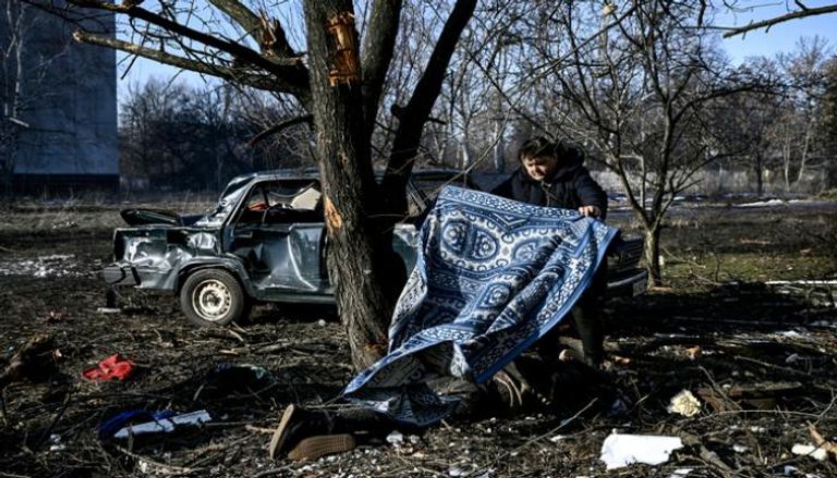 رجل يستخدم سجادة لتغطية جثة عقب قصف بلدة تشوغويف الأوكرانية