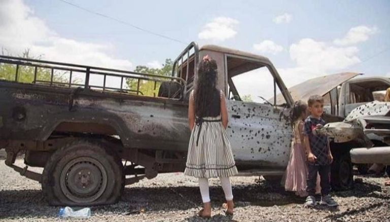 أطفال يمنيون يقفون أمام سيارة مدمرة جراء التفجير