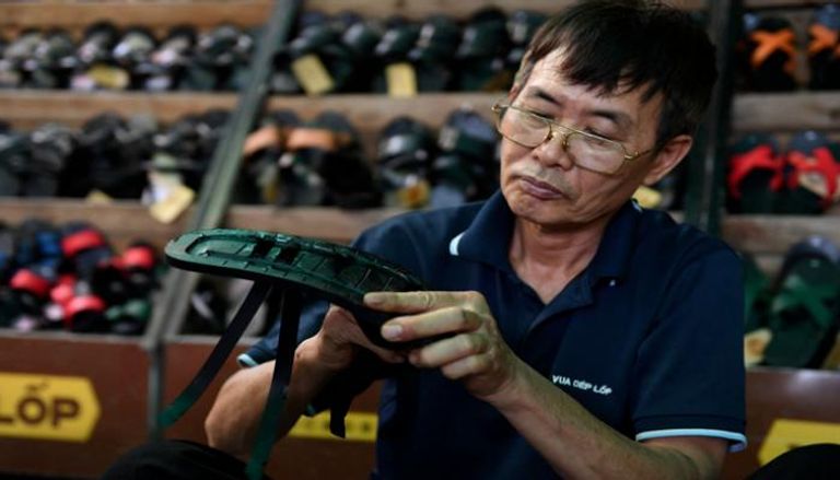 عامل يصنع حذاءً مطاطيًا في متجر في هانوي (أ ف ب)