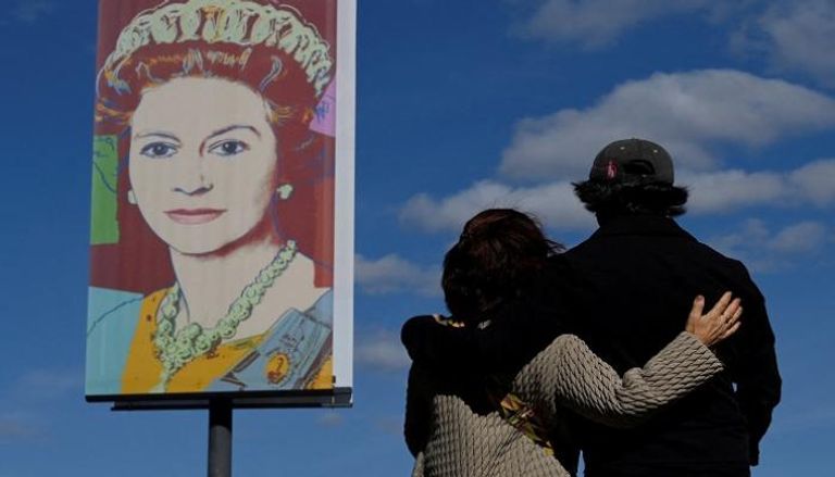 زوجان ينظران إلى صورة للملكة إليزابيث في أحد شوارع بريطانيا - رويترز