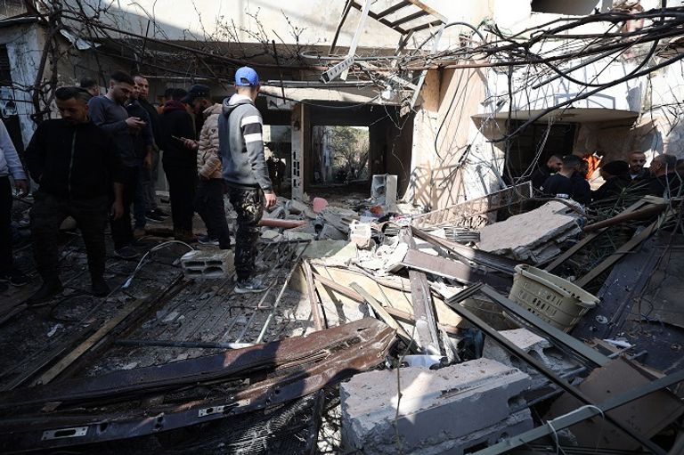 فلسطينيون يقفون أمام منزل دمرته القوات الإسرائيلية بمخيم جنين