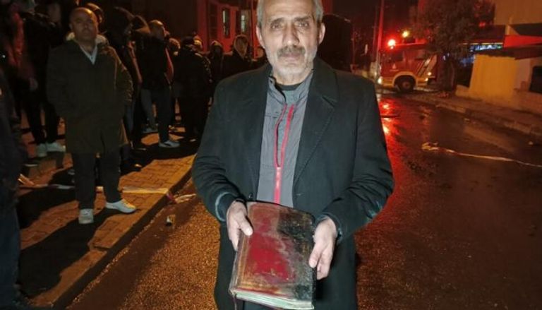 صاحب المنزل يحمل نسخة القرآن التي نجت من الحريق