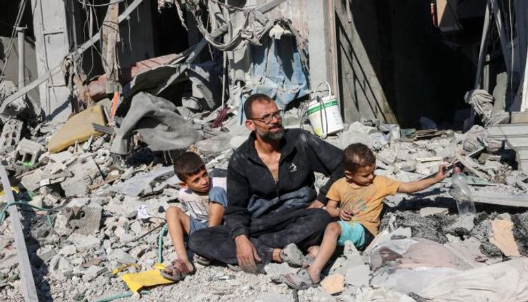 فلسطيني يجلس مع طفليه على أنقاض منزل مدمر 