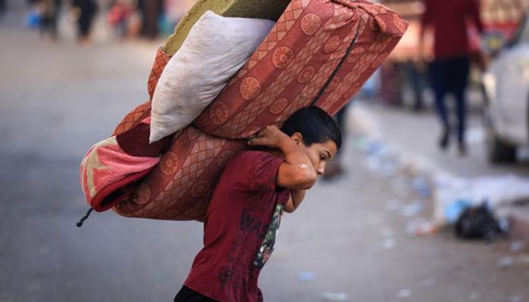 صبي يحمل مرتبة أثناء فرار الفلسطينيين مناطق أكثر أمانًا في غزة 