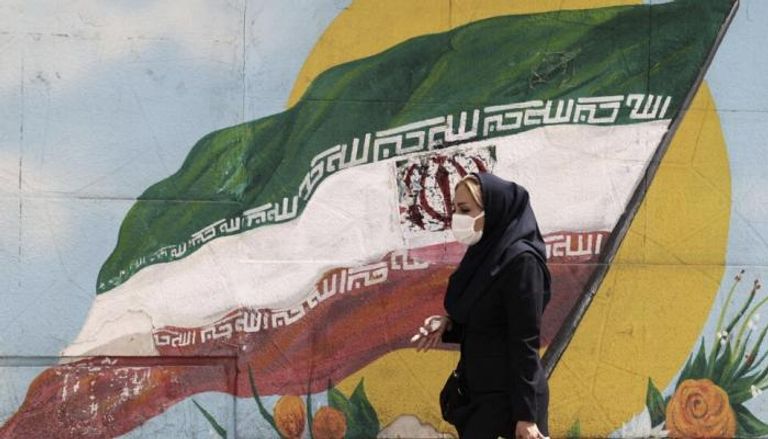 امرأة إيرانية تمشي أمام علم إيراني مرسوم على جدار في طهران