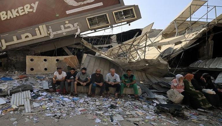 / أشخاص يجلسون أمام مخبز تم تدميره جزئيًا في غارة إسرائيلية على مخيم النصيرات وسط غزة