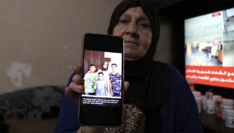لاجئة فلسطينية تعرض صورة لابنتها وأحفادها في غزة