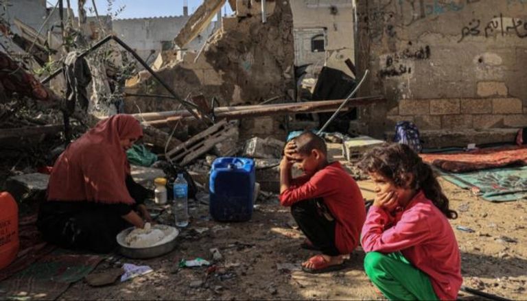فلسطينية وأحفادها وسط ركام منزلهم بغزة (أ ف ب)