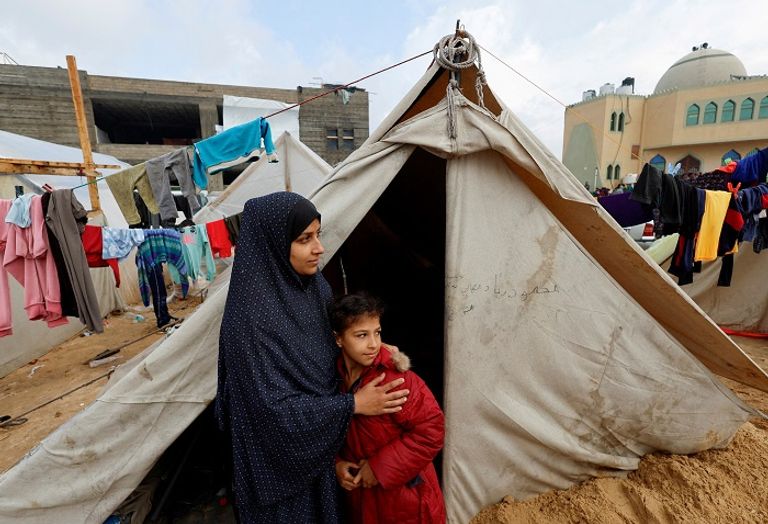 سيدة فلسطينية في رفح تحمي طفليها من الأمطار - رويترز