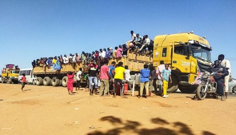 نازحون يصعدون على شاحنة تتحرك على طول طريق في ود مدني بالسودان