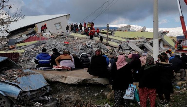 أشخاص يجلسون أمام مبنى منهار في أعقاب الزلزال الذي ضرب تركيا - رويترز