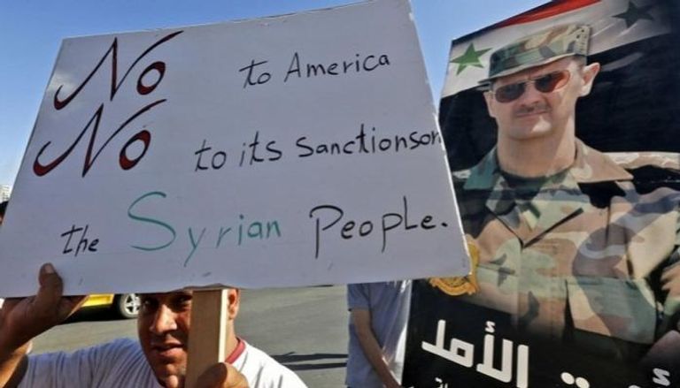 مواطن سوري يرقع لافتة ترفض العقوبات الأمريكية على سوريا - أرشيفية