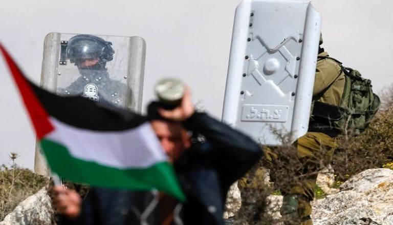 متظاهر فلسطيني يلوح بالعلم قرب قوات الأمن الإسرائيلية في مدينة نابلس  - أ ف ب