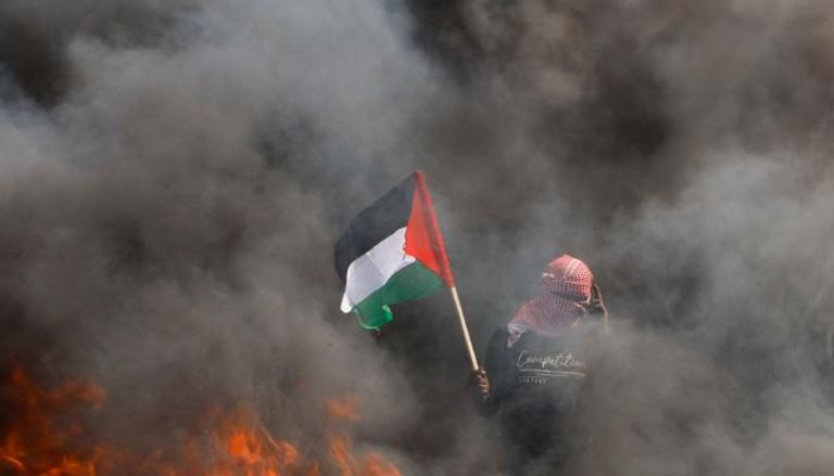 شاب فلسطيني يرفع علم بلاده وسط تصاعد أعمدة الدخان