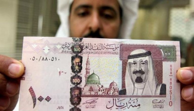 موظف بأحد البنوك يمسك ورقة نقد فئة 100 ريال سعودي -أرشيفية