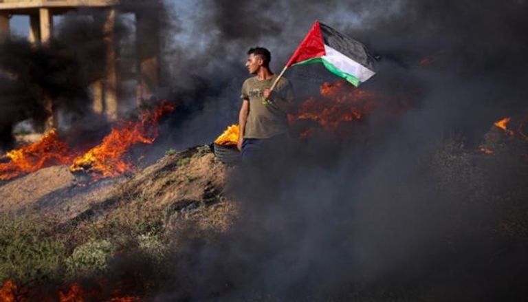 فلسطيني يحمل علما وسط النيران جراء المواجهات في جنين 