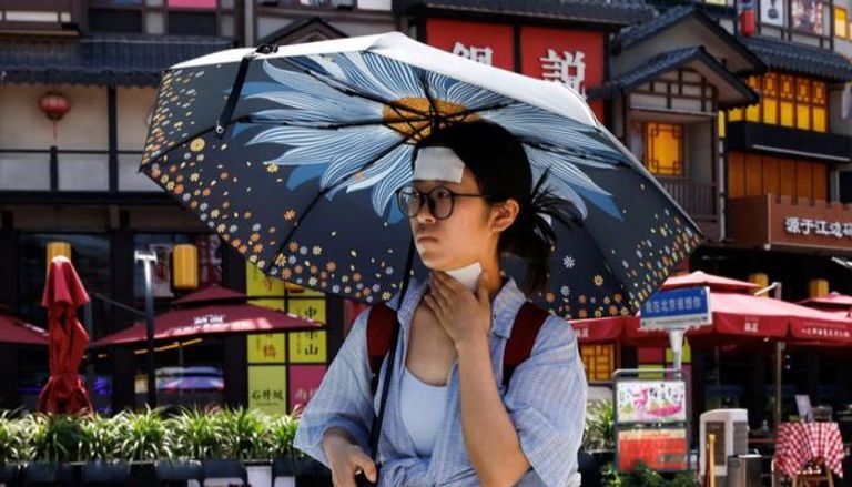امرأة تمشي في بكين وهي تضع كمادات باردة على جبهتها ورقبتها 