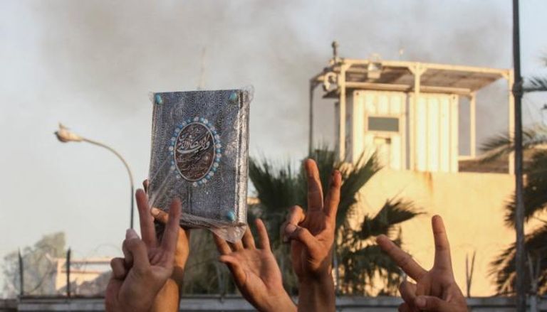متظاهر يحمل مصحفا مع تصاعد الدخان من مبنى السفارة السويدية ببغداد