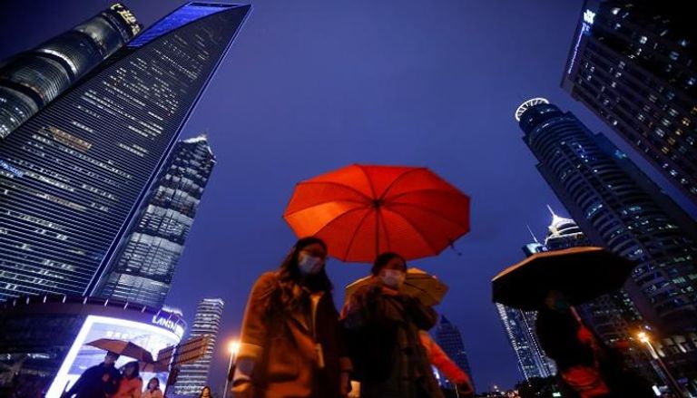 أشخاص يسيرون بمظلات في منطقة لوجيازوي المالية في شنغهاي- رويترز