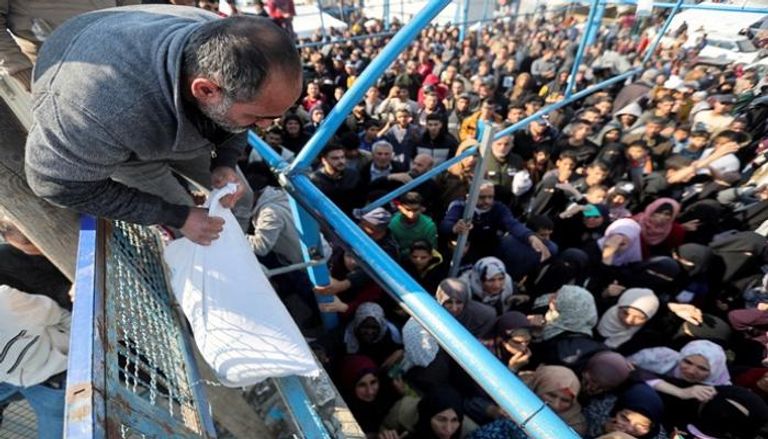 رجل فلسطيني يحمل كيس طحين بينما ينتظر آخرون استلامه من وكالة الأونروا