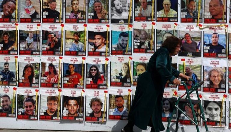 سيدة إسرائيلية تمر أمام حائط يحمل صورا لرهائن في غزة