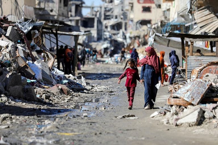 فلسطينيون يسيرون وسط دمار خلفه القصف الإسرائيلي على غزة - أرشيفية