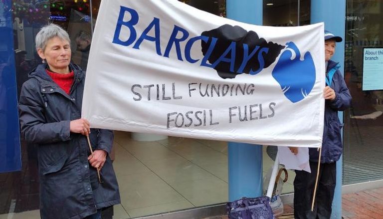متظاهرون يحملون لافتات تتهم بنك باركليز بتمويل الوقود الأحفوري