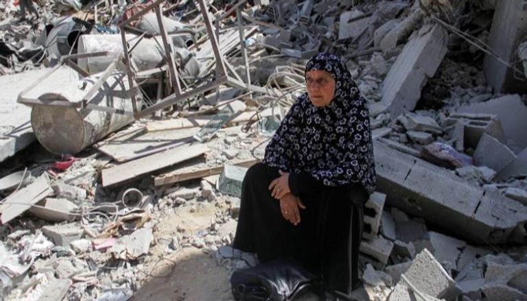 سيدة فلسطينية تجلس إلى جانب مبنى مدمر