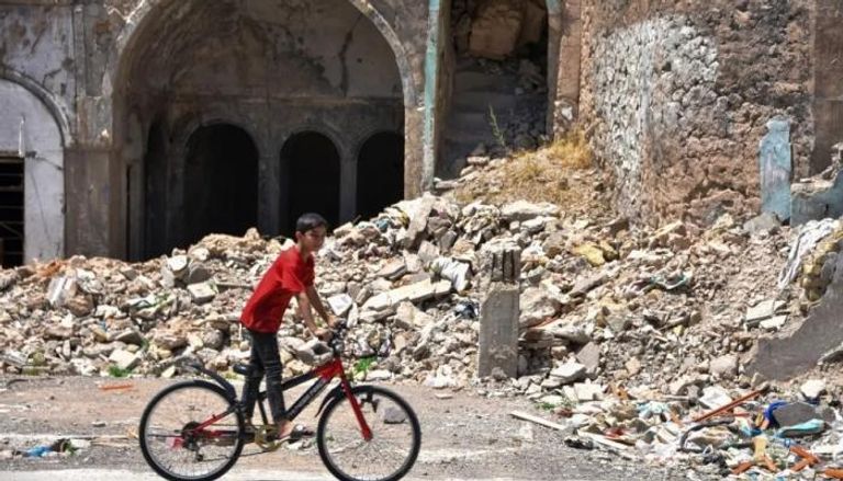 طفل عراقي يمر بدراجة أمام منزل مهدم من وقت الحرب