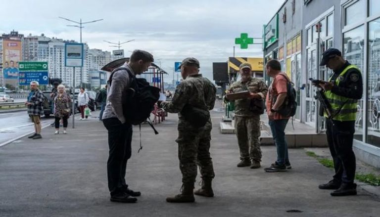 عناصر من الجيش الأوكراني يفحصون أوراق بعض الرجال خارج مترو الأنفاق