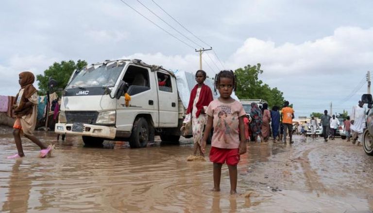 نازحون سودانيون يسيرون بالقرب من سيارات غمرتها مياه الفيضانات