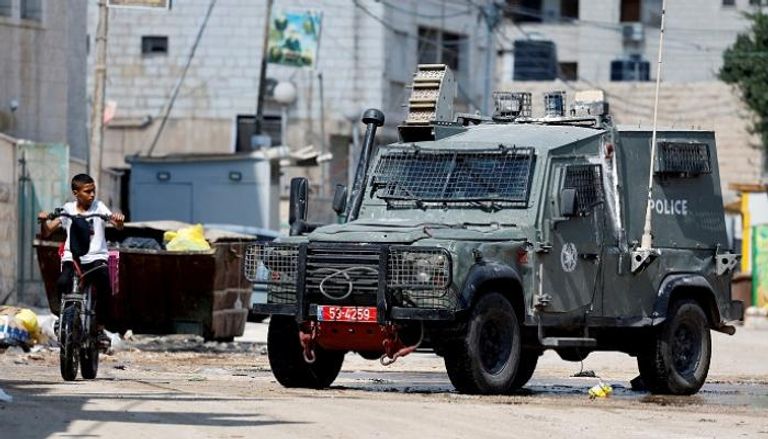 صبي فلسطيني في جنين يمر فوق دراجته قرب آلية إسرائيلية