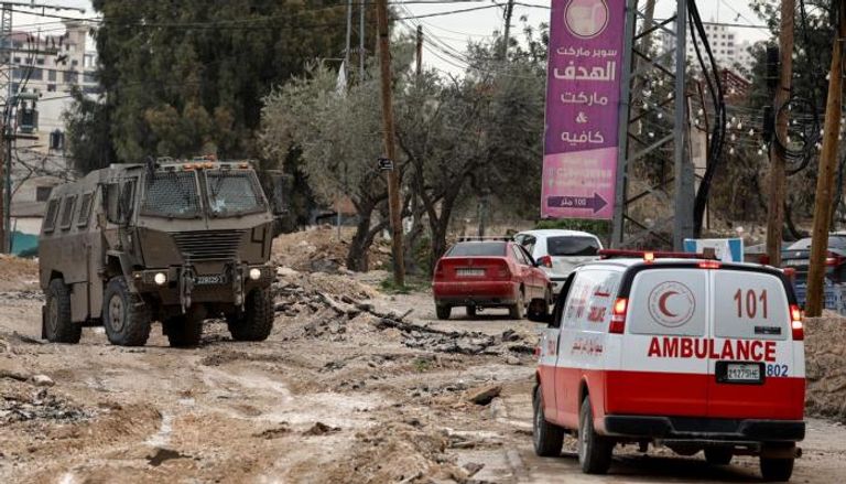 سيارة إسعاف فلسطينية تمر أمام آلية عسكرية إسرائيلية في جنين