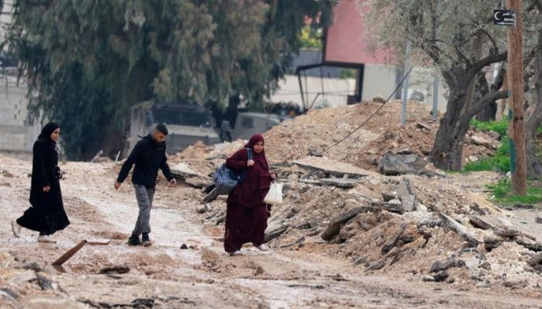 فلسطينيون يسيرون بطويق مدمر في جنين