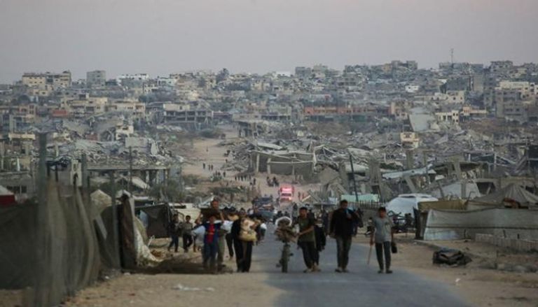 فلسطينيون يسيرون على طول الطريق أمام المباني المدمرة في خان يونس