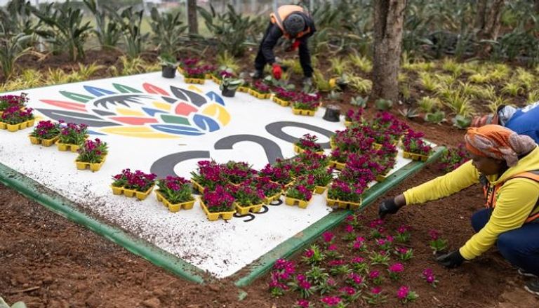 عمال يزرعون الزهور بجانب شعار قمة العشرين في جوهانسبرغ