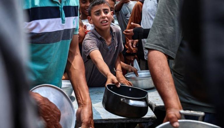 فلسطينيون يتجمعون لتلقي وجبة في نقطة توزيع طعام بمخيم النصيرات