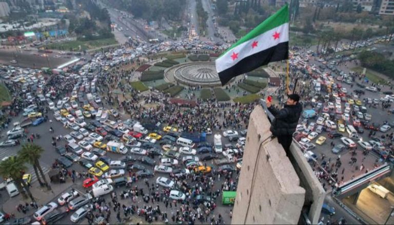 شاب يرفع العلم السوري الجديد في ميدان رئيسي في دمشق