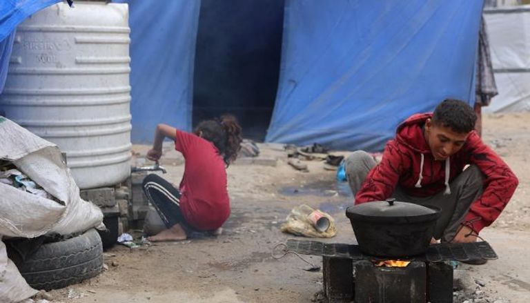 فلسطينيون في مخيم نزوح وسط أنقاض مبنى في مدينة غزة