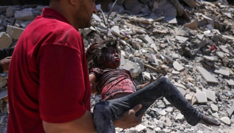 فلسطيني يحمل طفلة مصابة في قصف إسرائيلي بغزة