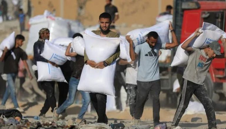 فلسطينيون يحملون أجولة طحين توزع بقطاع غزة